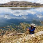 Person in White Skirt and Blue Top Relaxing by Tranquil Lake with Wildflowers