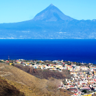 Scenic coastal town with white buildings, blue mountains, and snow-capped peak