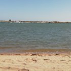 Person in hat on sandy beach gazes at sea with rocks, birds.