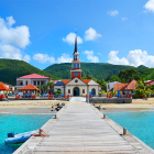 Vibrant coastal village with churches and houses nestled by green hills, sandy beach, and blue sea