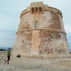 Fantastical sand castle-like lighthouse on coastal rock with grand staircases and flora under serene sky