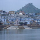 Fantastical cityscape with sandy beehive buildings and blue domes reflected in water against mountain