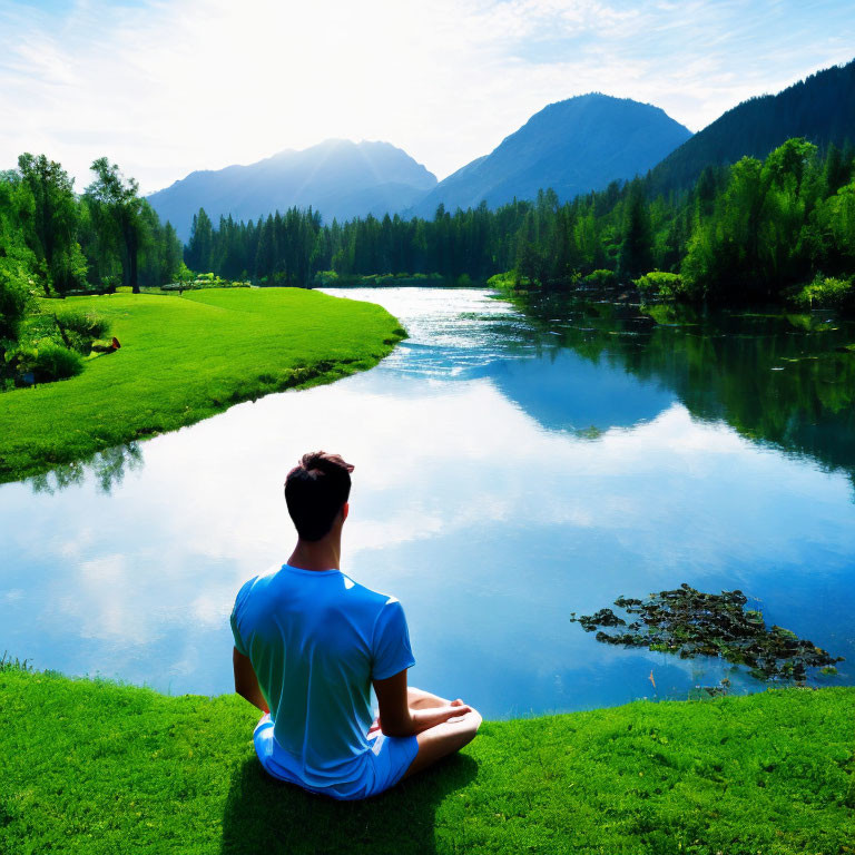 Person in Blue Shirt Relaxing by Serene River amid Lush Greenery