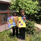 Women in floral garden holding matching paintings