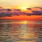 Sailboats on shimmering water at sunset with vibrant orange sun