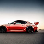 Red sports car with rear wing and black rims parked on asphalt road at dusk