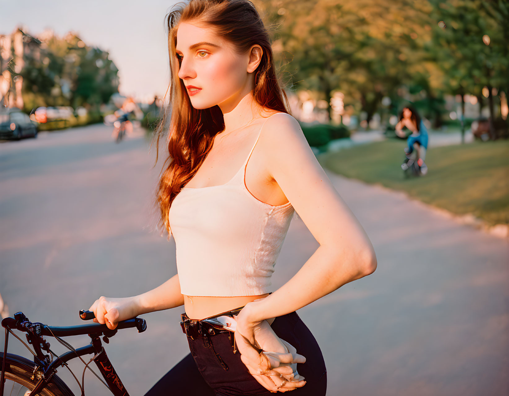 Young woman with long brown hair holding a bicycle at sunset in park