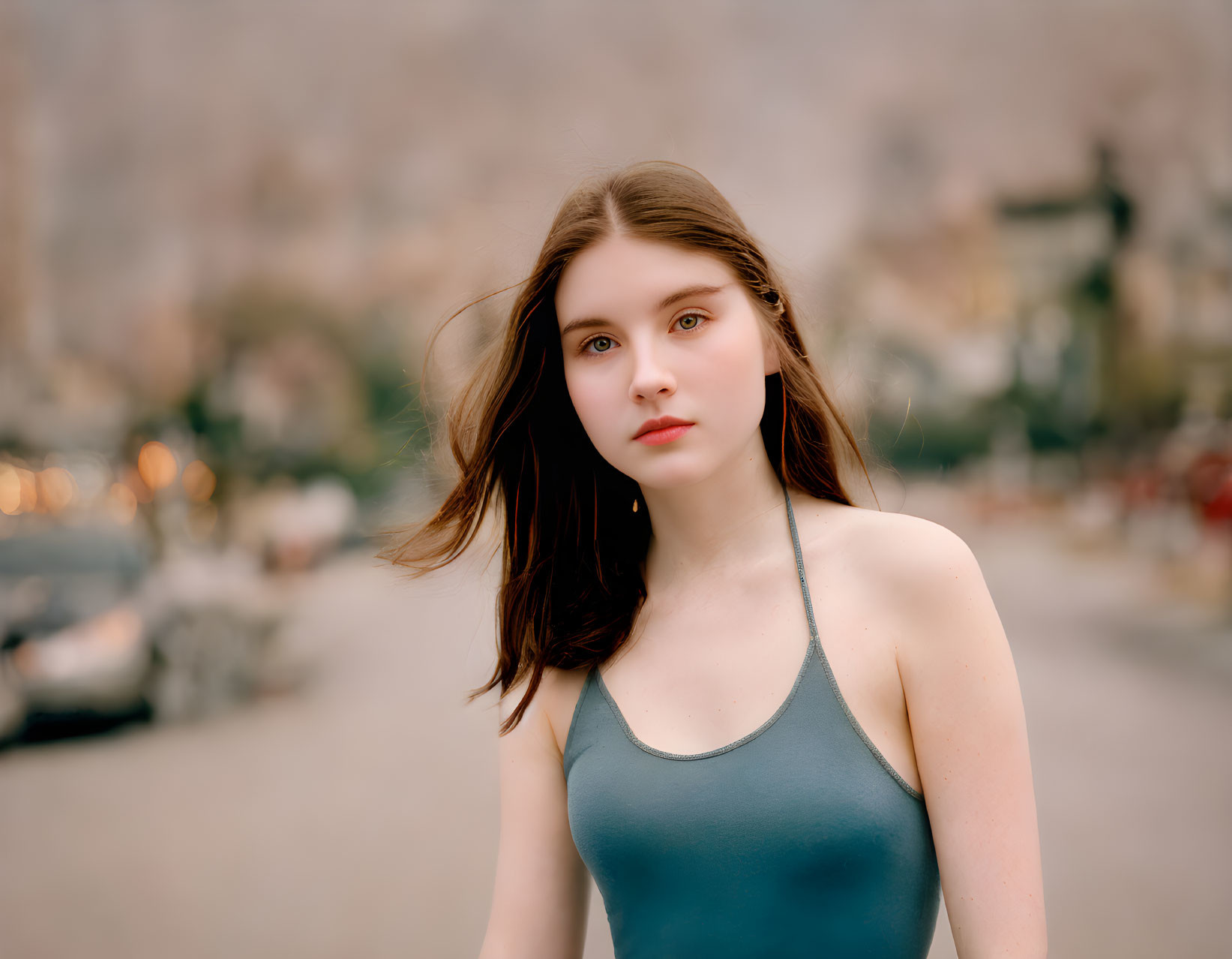 Young woman with flowing hair in grey top outdoors with blurred background