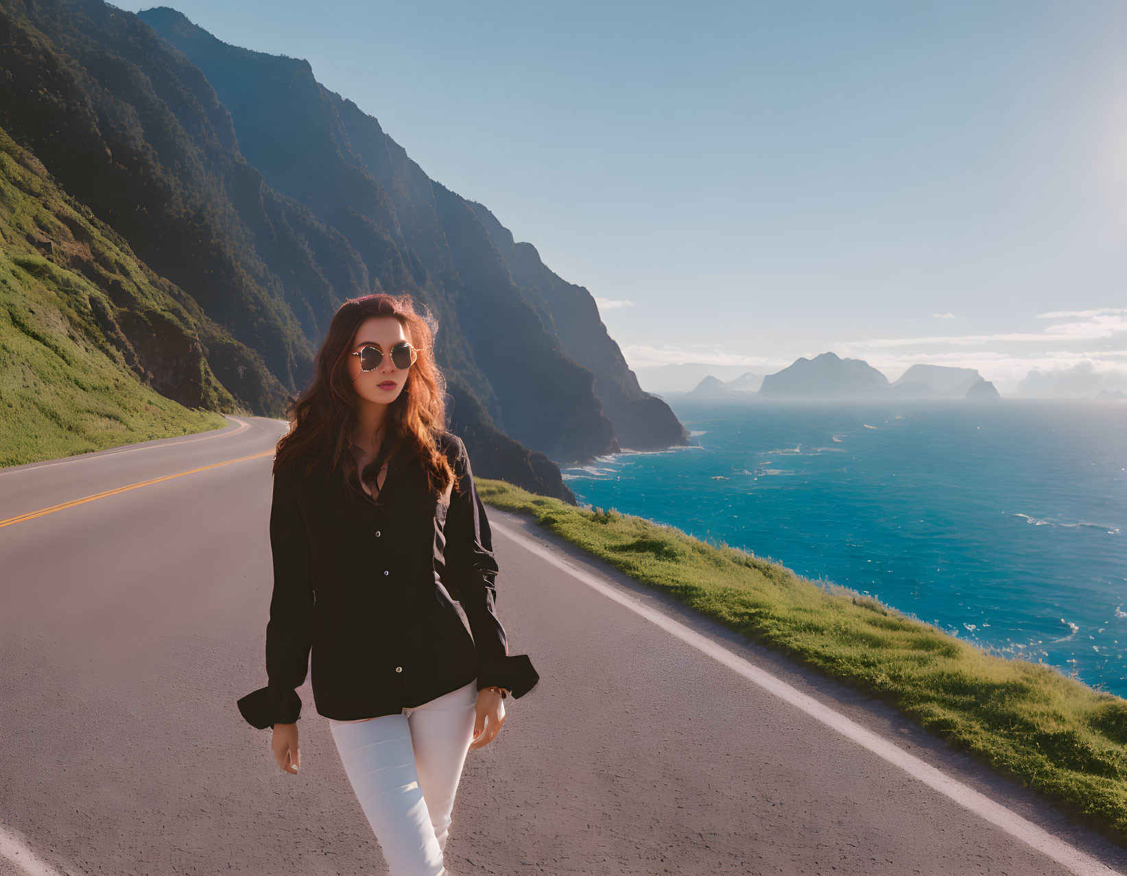 Woman in sunglasses walks coastal road with ocean and cliffs.