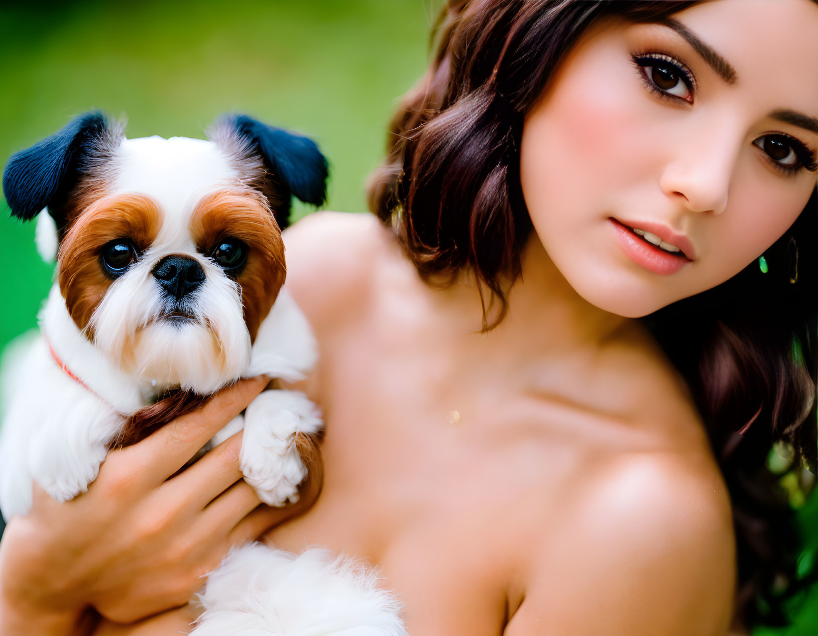 Woman with makeup holding small shih tzu dog in front of blurred green background