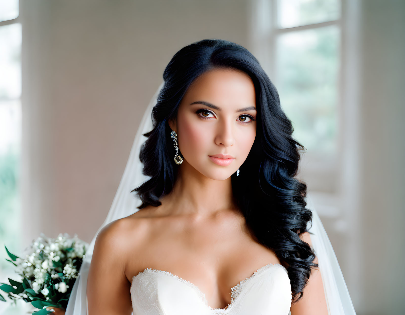 Dark-haired bride in white gown with bouquet and veil, looking at camera