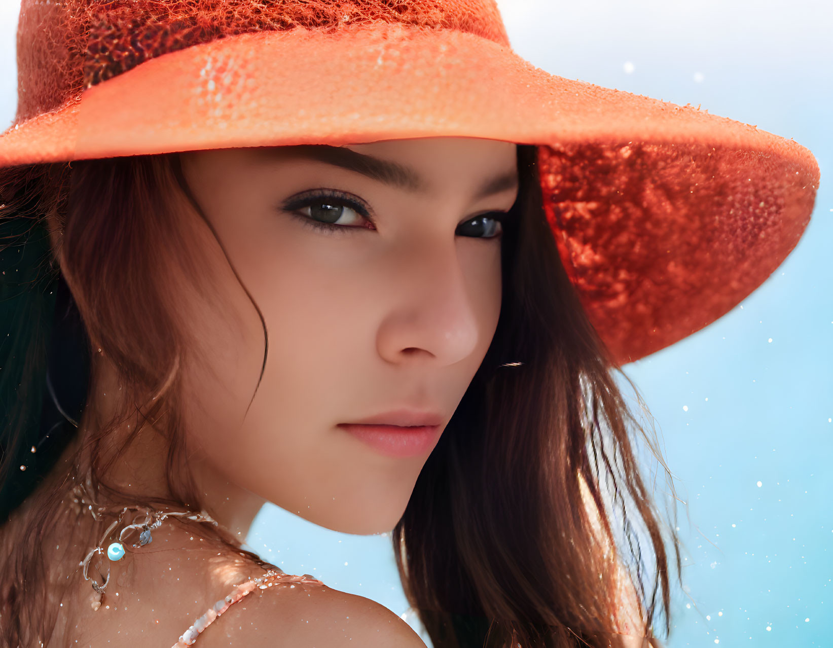 Woman in orange hat with water droplets on skin against blue backdrop