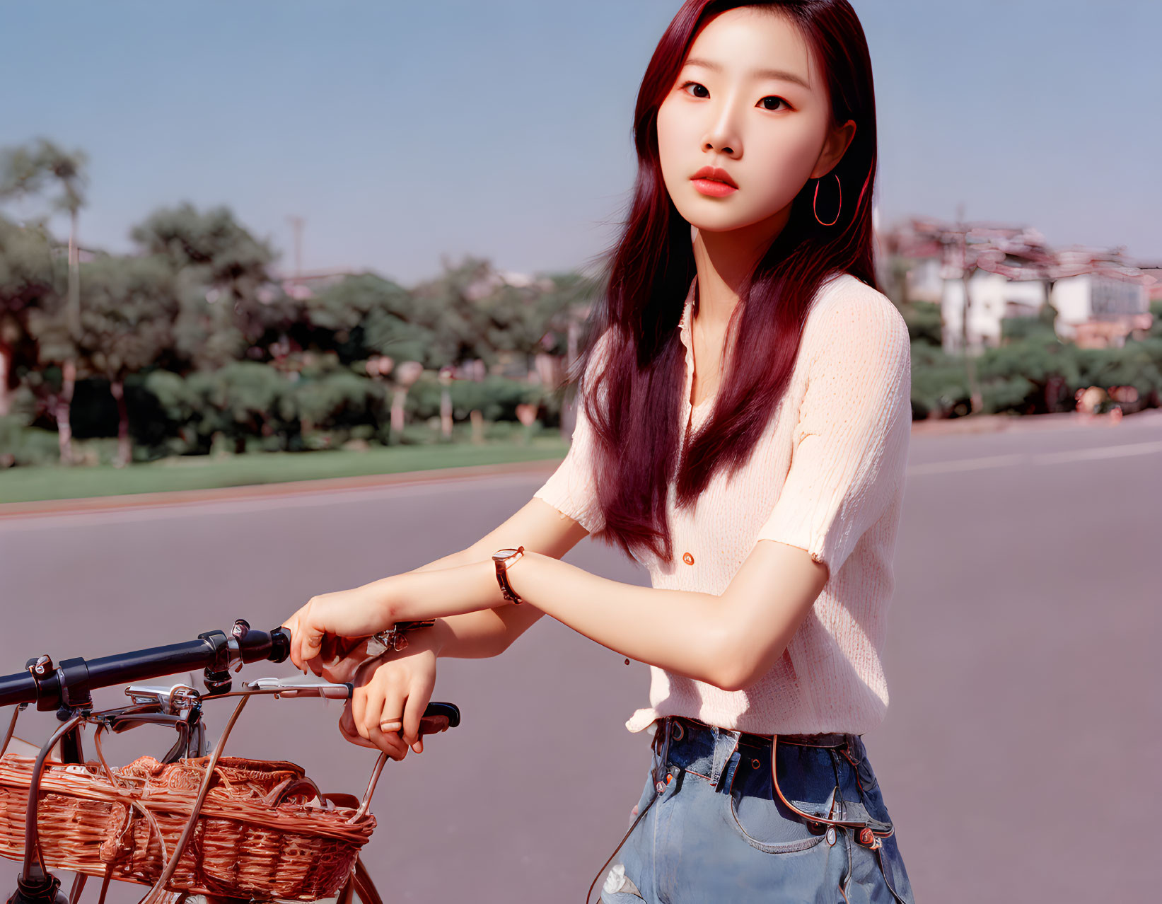 Young woman with purple hair in white top and denim shorts holding bike on tree-lined road