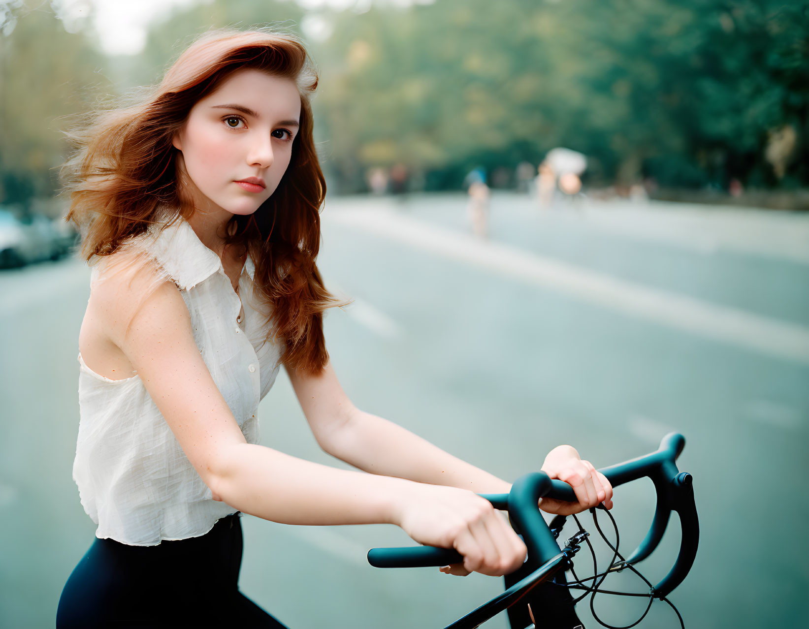 Young woman in white blouse on bike, looking back on tree-lined street