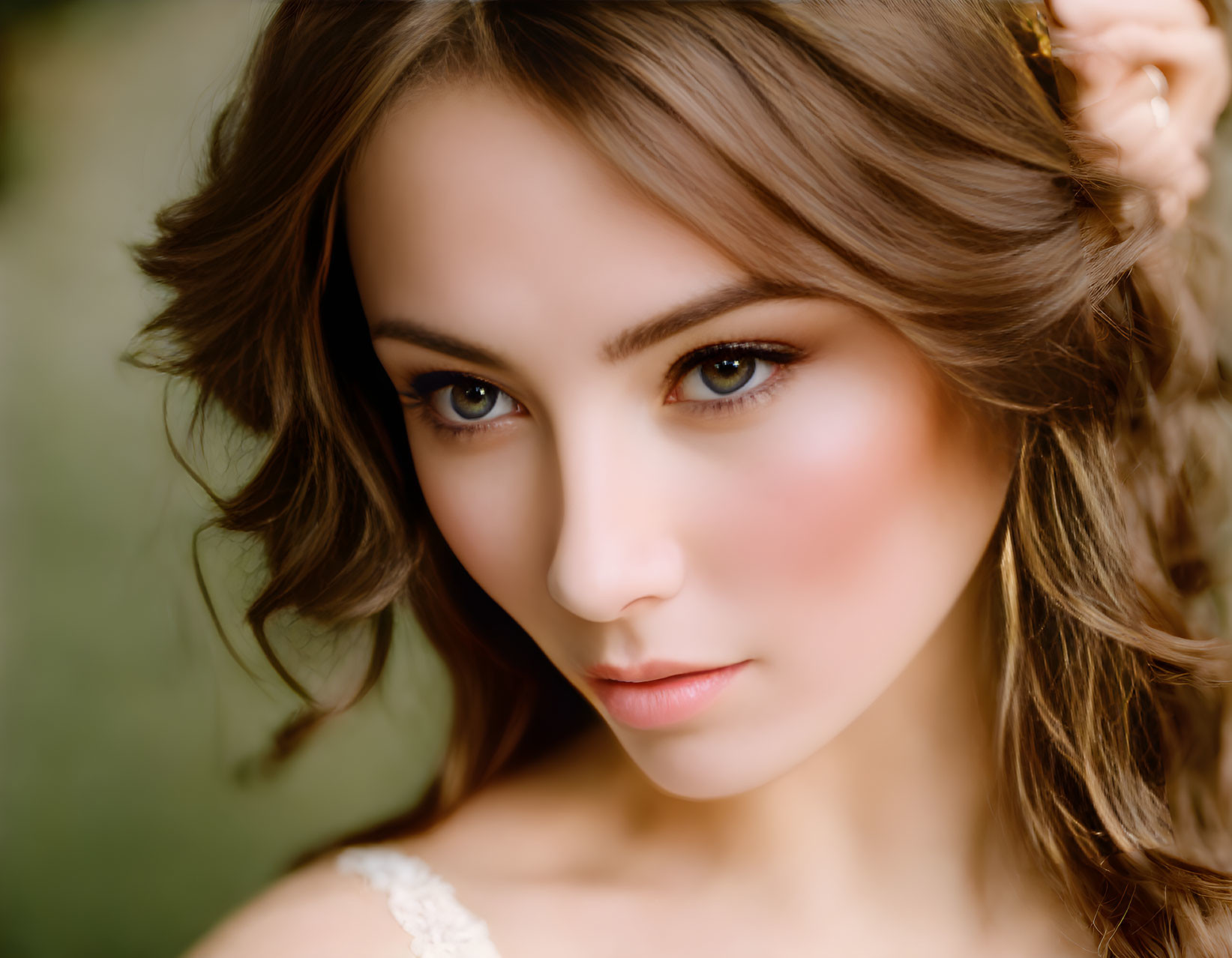 Woman with subtle makeup, wavy hair, and flower accessory gazes at viewer