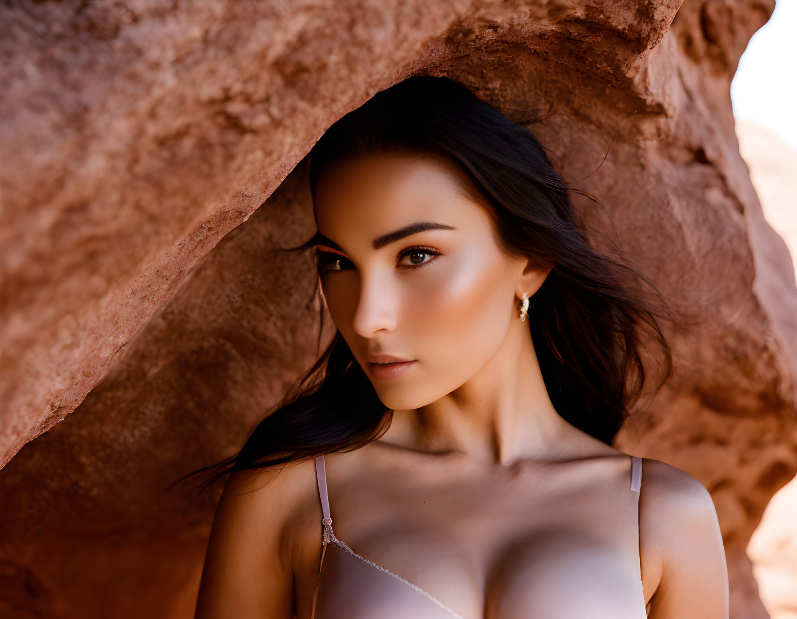 Dark-haired woman under rock arch exudes elegance in natural setting