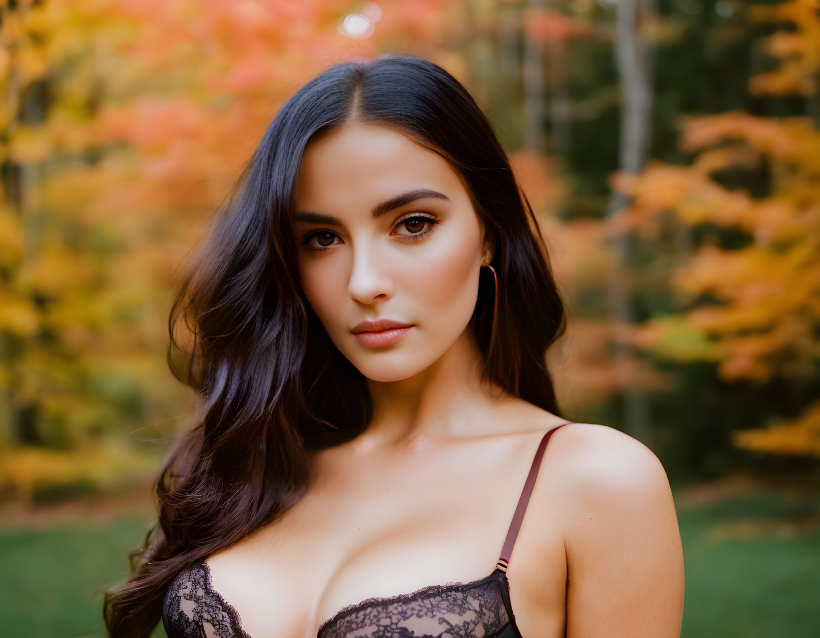 Dark-haired woman in lace top among autumn leaves.