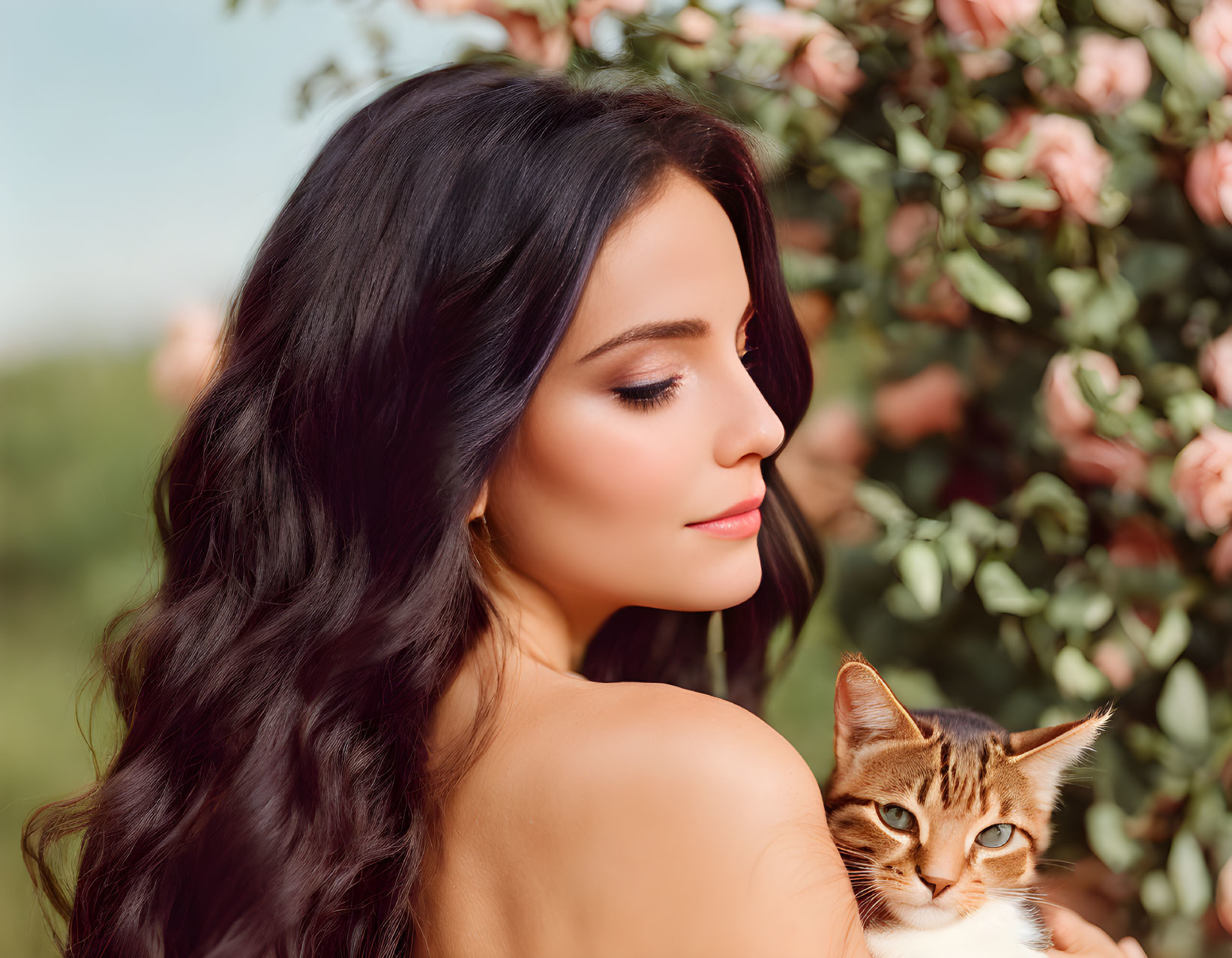 Dark-haired woman holding tabby cat among pink flowers.