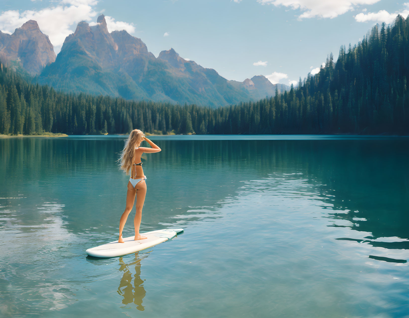 Person on paddleboard in mountain lake admiring forested peaks