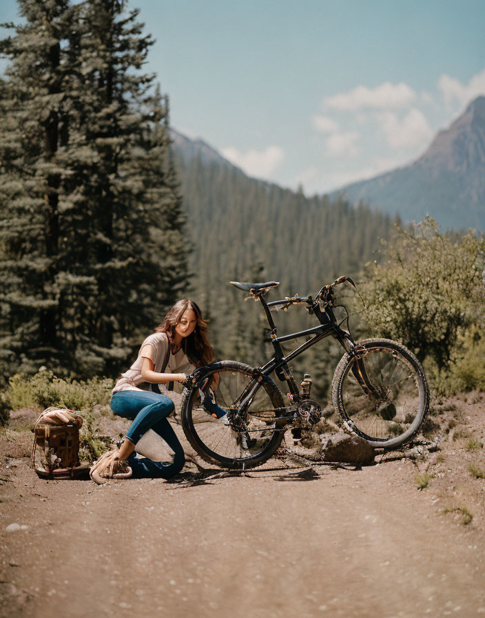 Woman crouching by bicycle on dirt trail with lush greenery and mountains in background