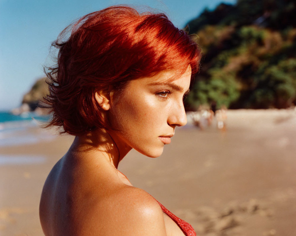 Red-haired woman on sunny beach with people and trees in background