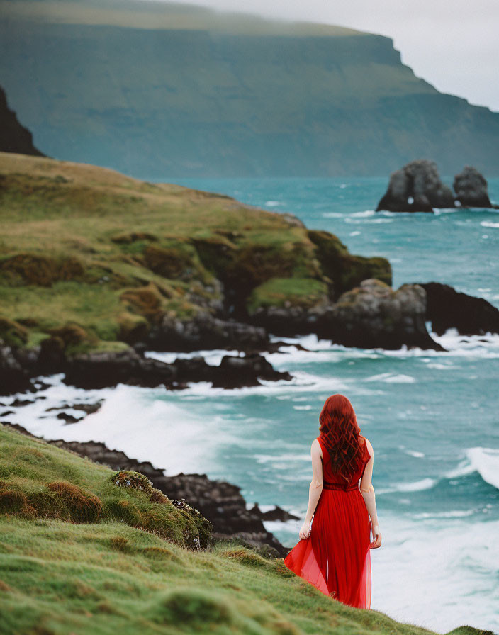 Red-haired woman in flowing dress on cliff overlooking turbulent ocean