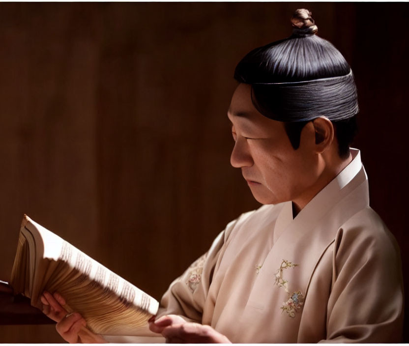 Traditional East Asian attire person with topknot hairstyle reading old book