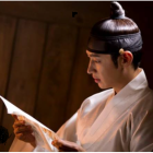 Traditional East Asian attire person with topknot hairstyle reading old book