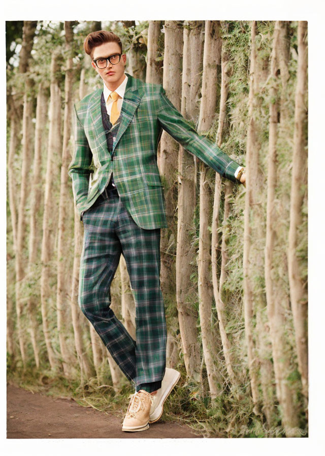 Fashionable individual in green plaid suit and glasses among tall tree trunks