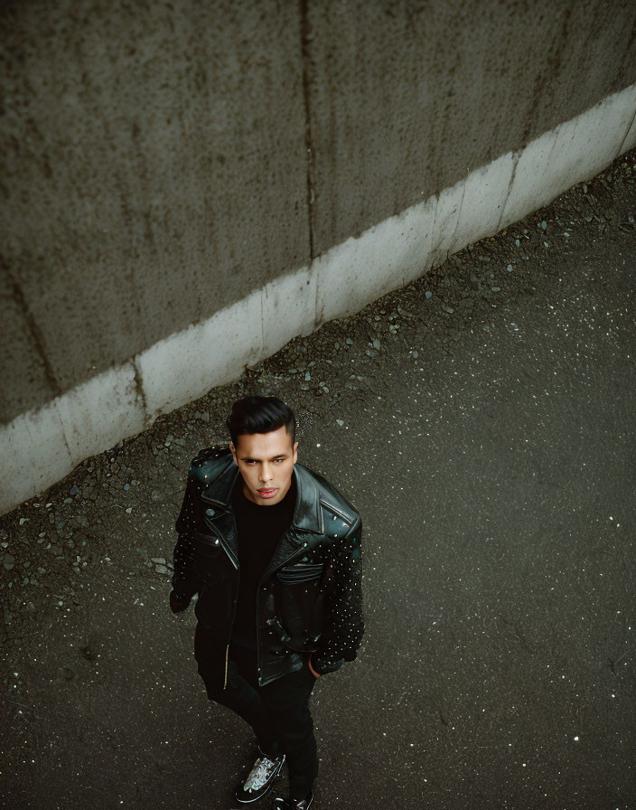 Studded black leather jacket man on asphalt road next to concrete wall