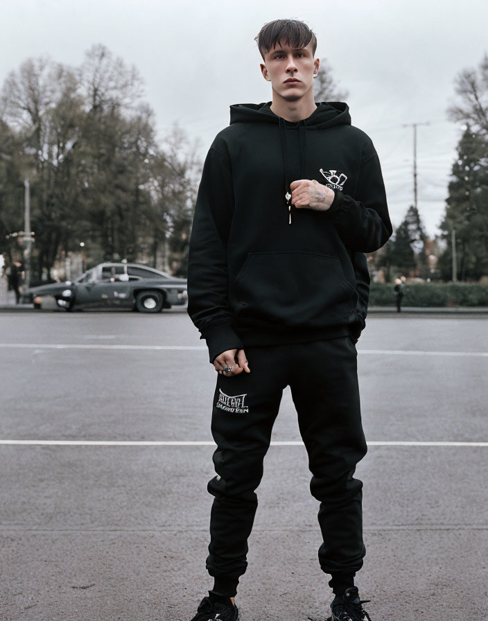 Young man in black hoodie and sweatpants on city street with cars