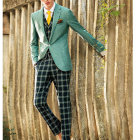 Fashionable individual in green plaid suit and glasses among tall tree trunks