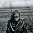 Man in sunglasses and camo jacket against dystopian cityscape