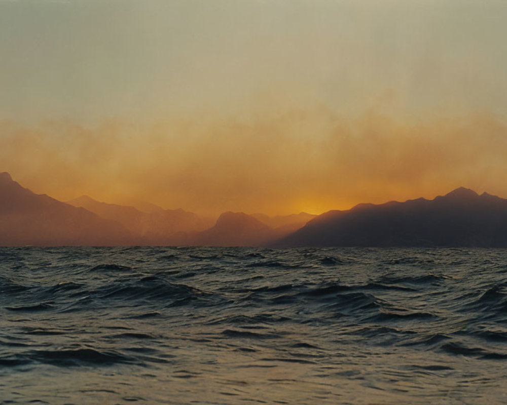 Scenic sunset over hazy mountain range and choppy sea waters