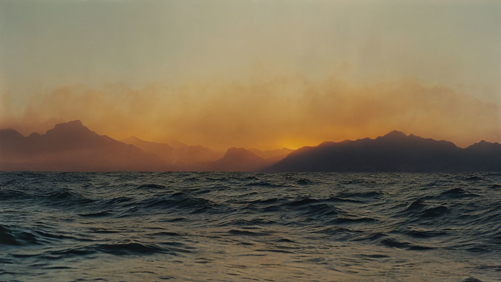 Scenic sunset over hazy mountain range and choppy sea waters