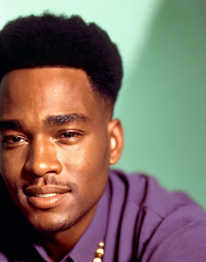 Smiling man with high-top fade in purple shirt on green background