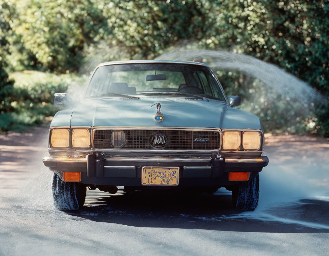 Vintage Blue Car Spraying Water on Wet Road Amid Greenery