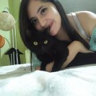 Woman with expressive eyes embracing black cats on the ground