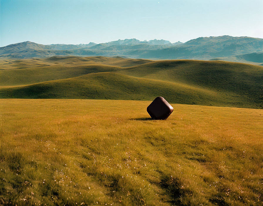 Brown Dice-Shaped Object on Green Hillside under Blue Sky