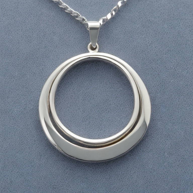 Circular Silver Pendant on Chain Against Gray Background