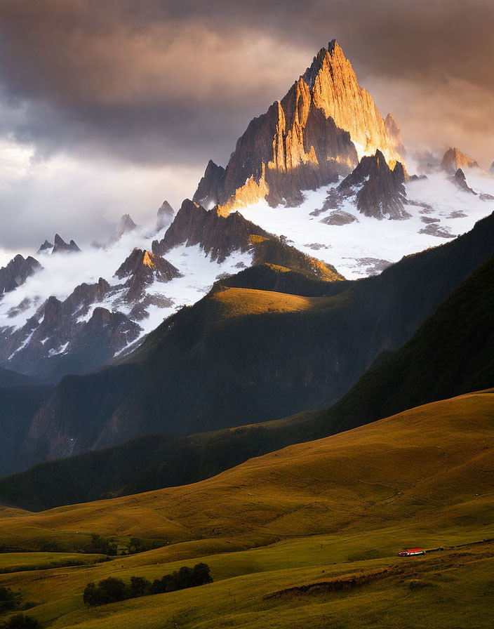 Dramatic sunset light on sharp mountain peak and rolling green hills with small house under cloudy sky