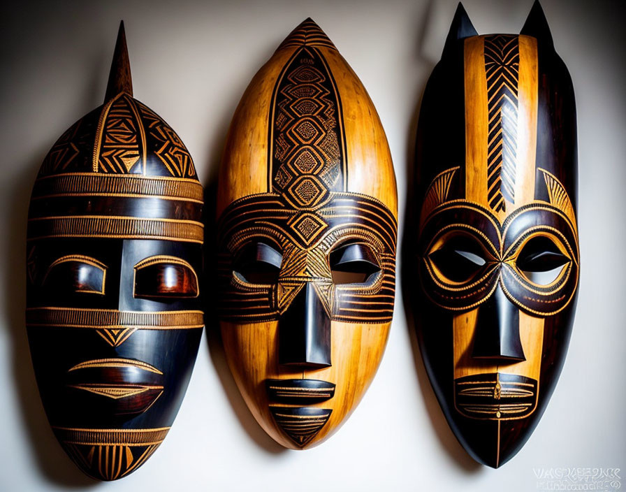 Three ornate wooden tribal masks with intricate designs on white wall