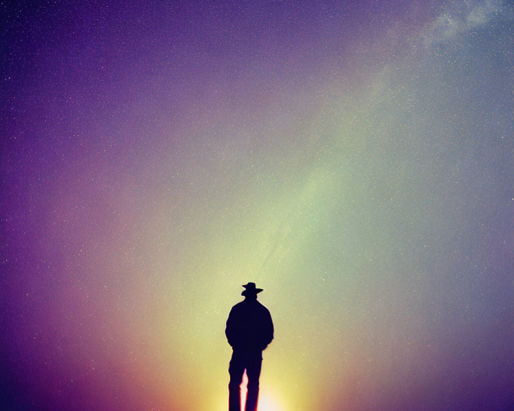 Person silhouette with hat against starry twilight sky and Milky Way in sunset orange to deep purple gradient