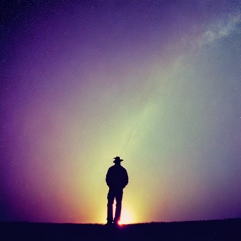 Person silhouette with hat against starry twilight sky and Milky Way in sunset orange to deep purple gradient