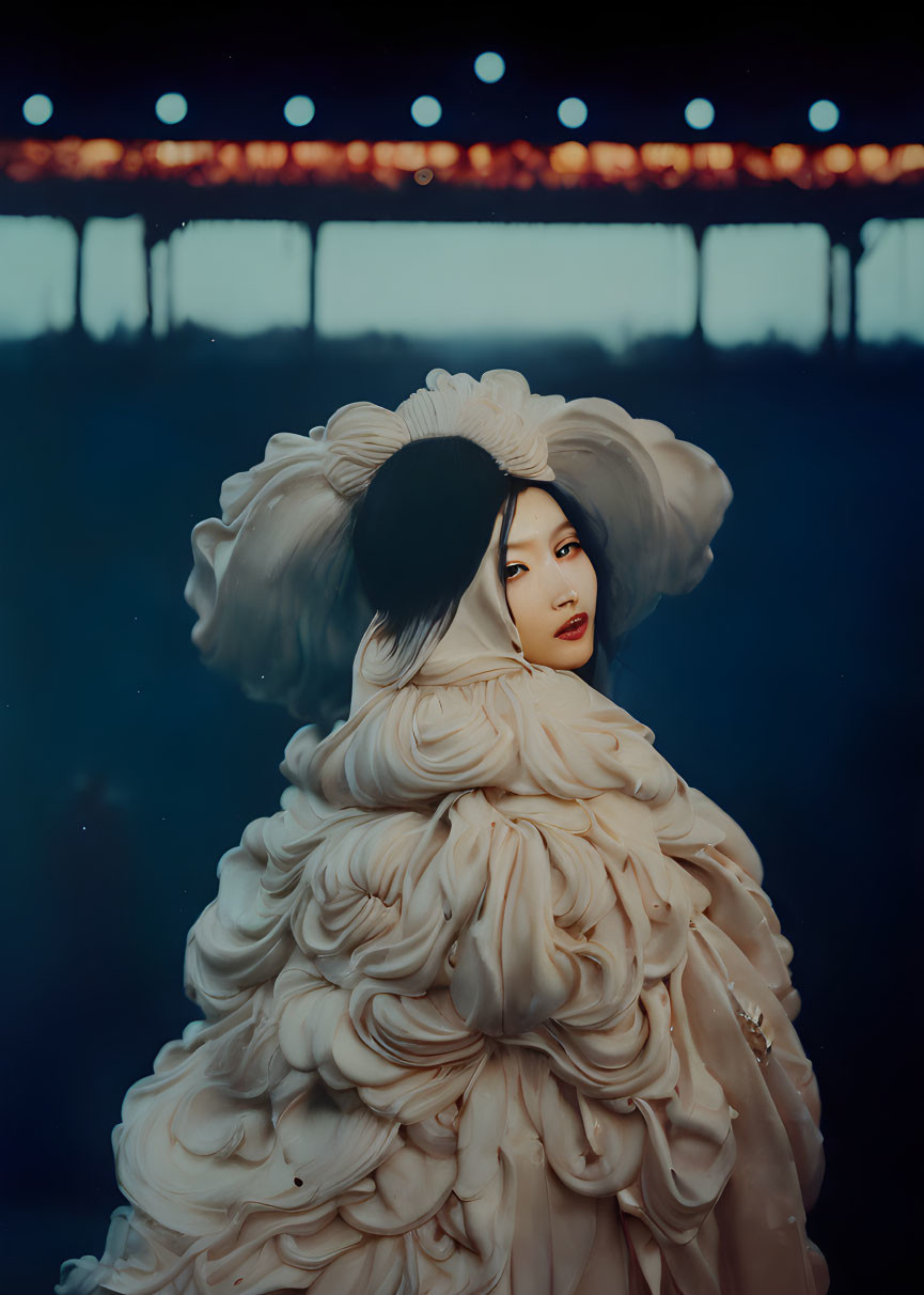 Dark-haired woman in ruffled light gown glances back in dim setting