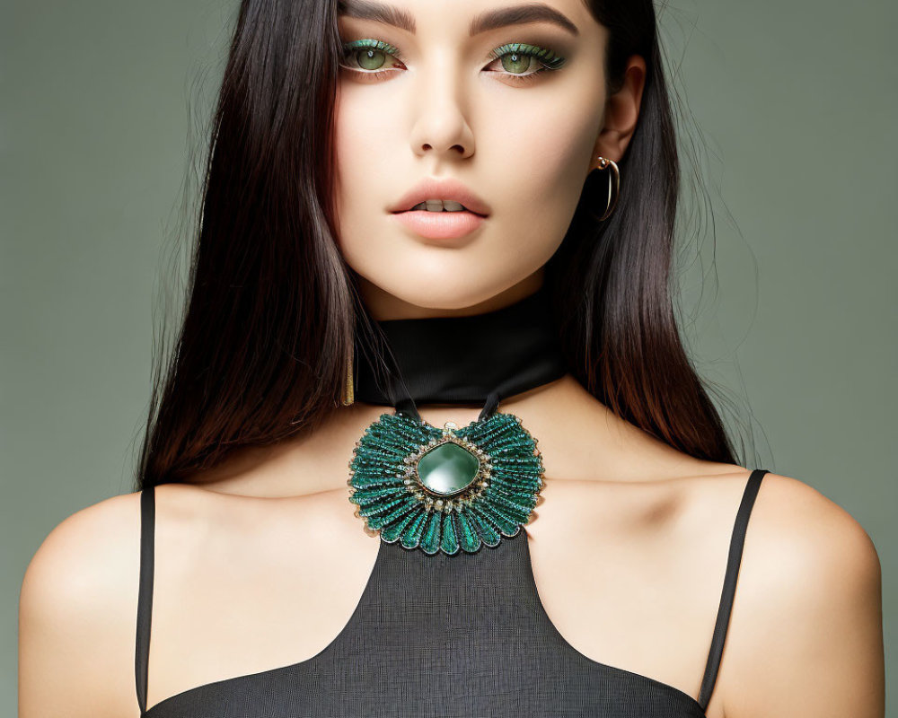 Dark-haired woman in black top with green necklace and hoop earrings on green background.