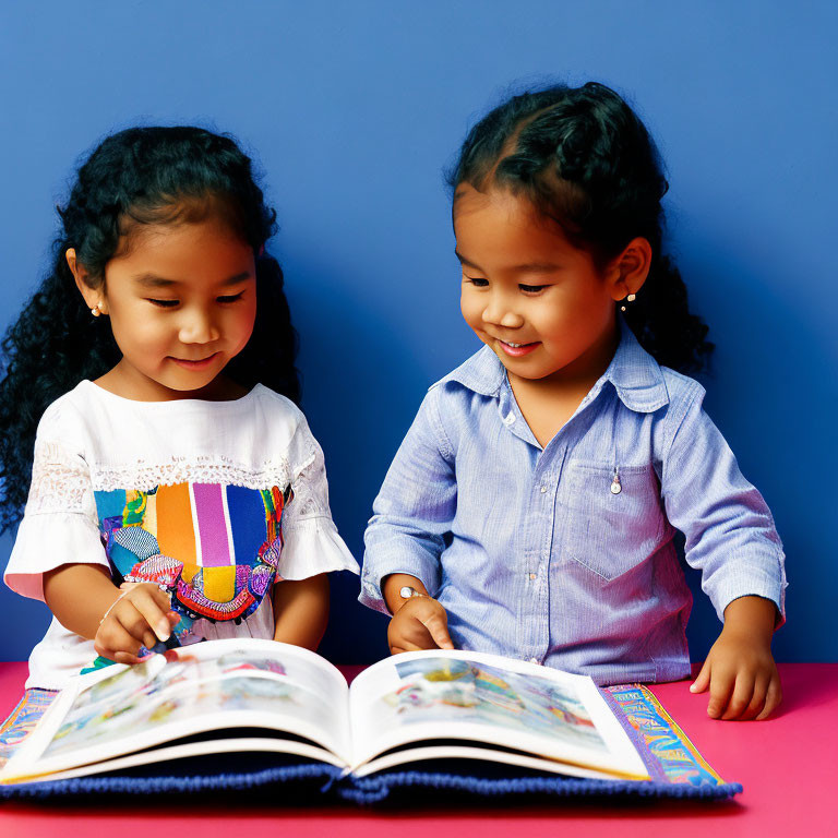 Young girls smiling at open book on blue background