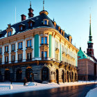 Baroque-style building with turquoise and beige facade and black dome next to towered structure, set in