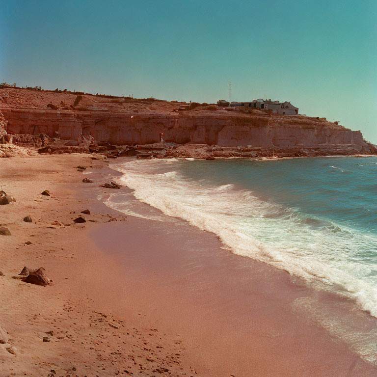 Tranquil sandy beach with gentle waves, cliff, and house overlooking serene view