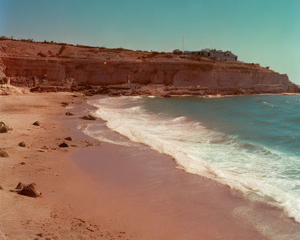 Tranquil sandy beach with gentle waves, cliff, and house overlooking serene view